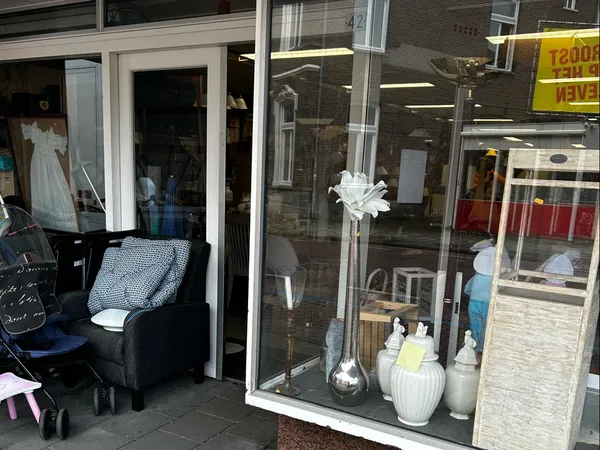 Etalage van kringloopwinkel met witte bloem in vaas en huishoudelijke spullen uitgestald in raam