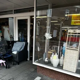 Etalage van kringloopwinkel met witte bloem in vaas en huishoudelijke spullen uitgestald in raam