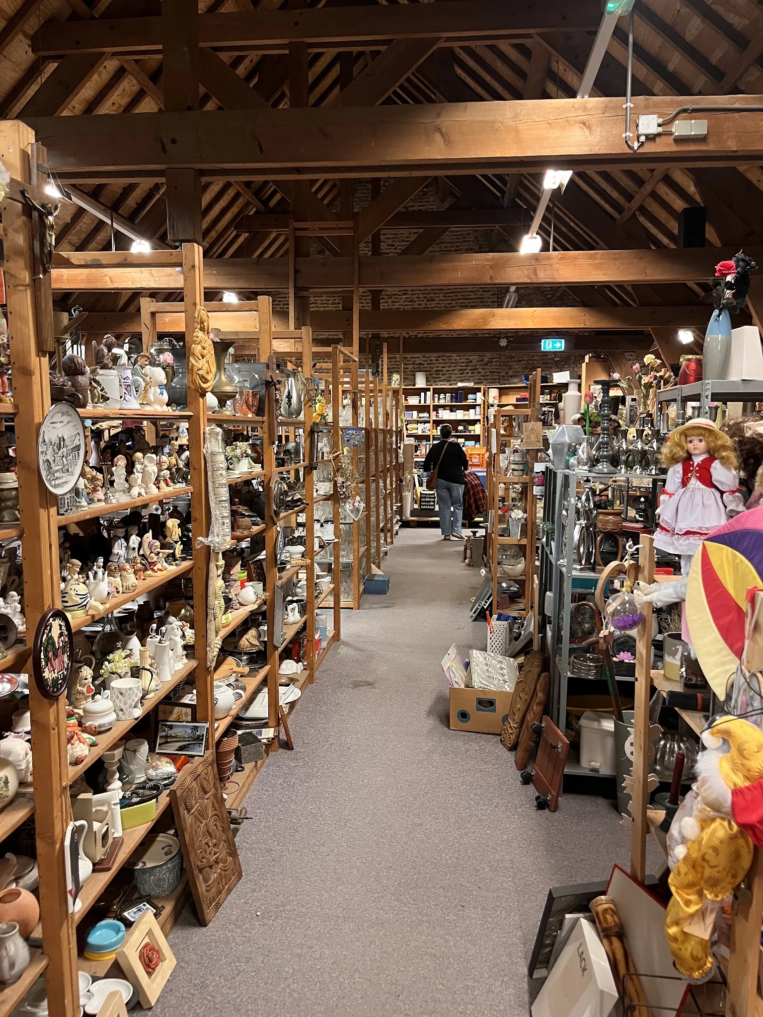 Winkelinterieur met houten stellingen vol decoratieve artikelen, beeldjes en huisraad; lopen pad door het midden
