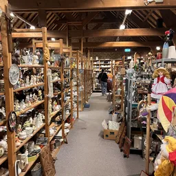 Winkelinterieur met houten stellingen vol decoratieve artikelen, beeldjes en huisraad; lopen pad door het midden