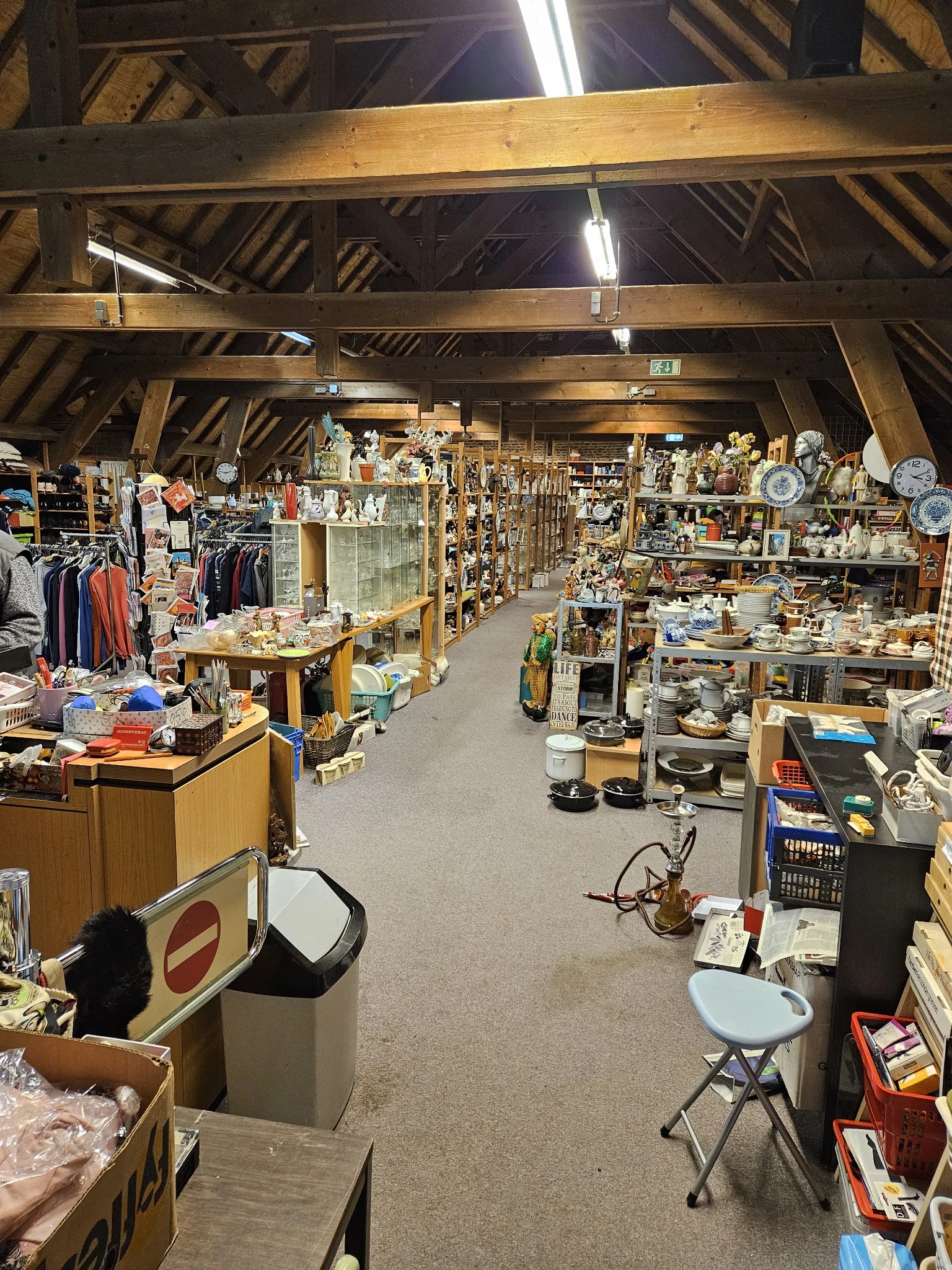 Overzicht van de winkelvloer met stellingen vol huishoudartikelen, servies, decoratie en kleding aan de linkerkant