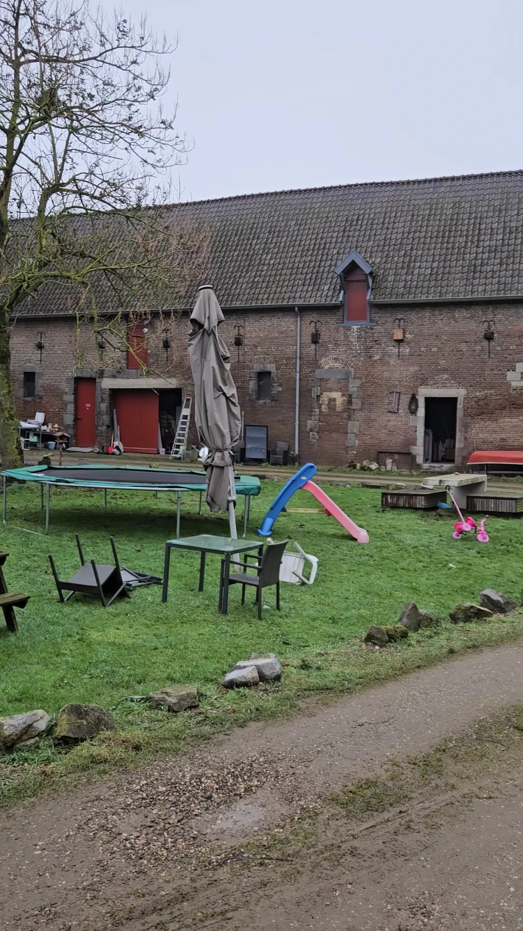 Grasveld met speeltoestellen, trampolines en tuinmeubilair naast een bakstenen gebouw
