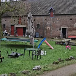 Grasveld met speeltoestellen, trampolines en tuinmeubilair naast een bakstenen gebouw