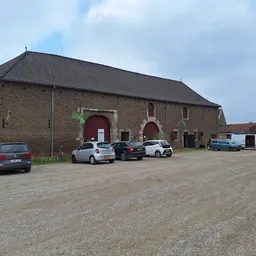 Bakstenen kringloopwinkel met rode deuren en parkeerterrein met auto's ervoor