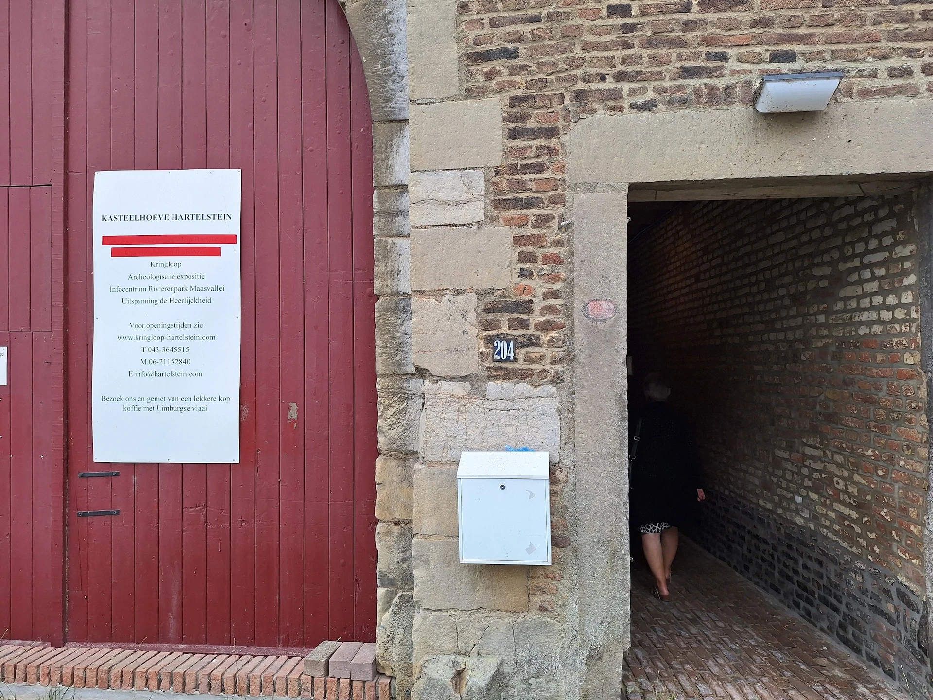 Rode deur met informatiebord en bakstenen muur met deuropening van kringloopwinkel