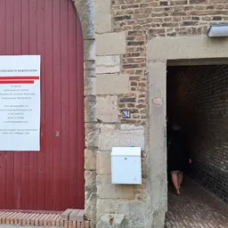 Rode deur met informatiebord en bakstenen muur met deuropening van kringloopwinkel
