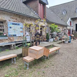 Voorkant van kringloopwinkel met bakstenen gevel, houten zitbanken op het terrein en tuinartikelen
