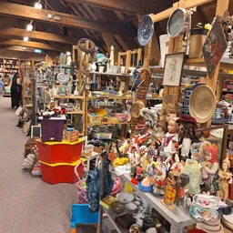 Winkelvloer van kringloopwinkel met diverse rekken, stellingen en uitgestalde spullen zoals servies, decoratie en gebruiksart