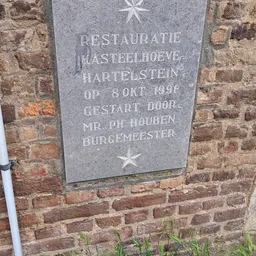 Gedenksteen aan bakstenen muur met inscriptie over restauratie Kasteelhoeve Hartelstein