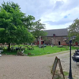 Bakstenen kerk met groene grasvelden, bomen en picknicktafels op het terrein