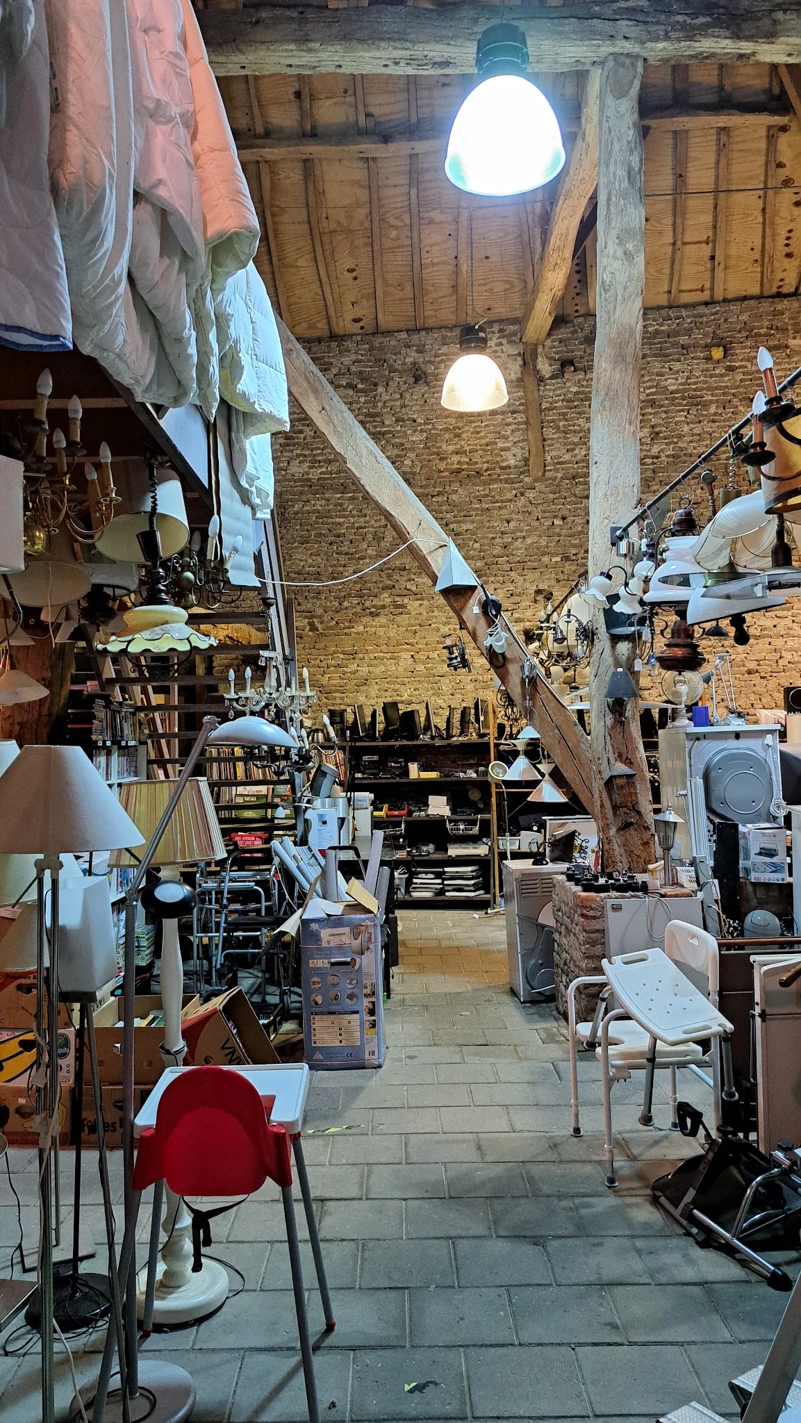 Binnenaanzicht van kringloopwinkel met diverse meubels, lampen, rekken en huishoudelijke spullen op houten vloer