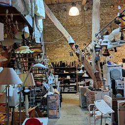 Binnenaanzicht van kringloopwinkel met diverse meubels, lampen, rekken en huishoudelijke spullen op houten vloer
