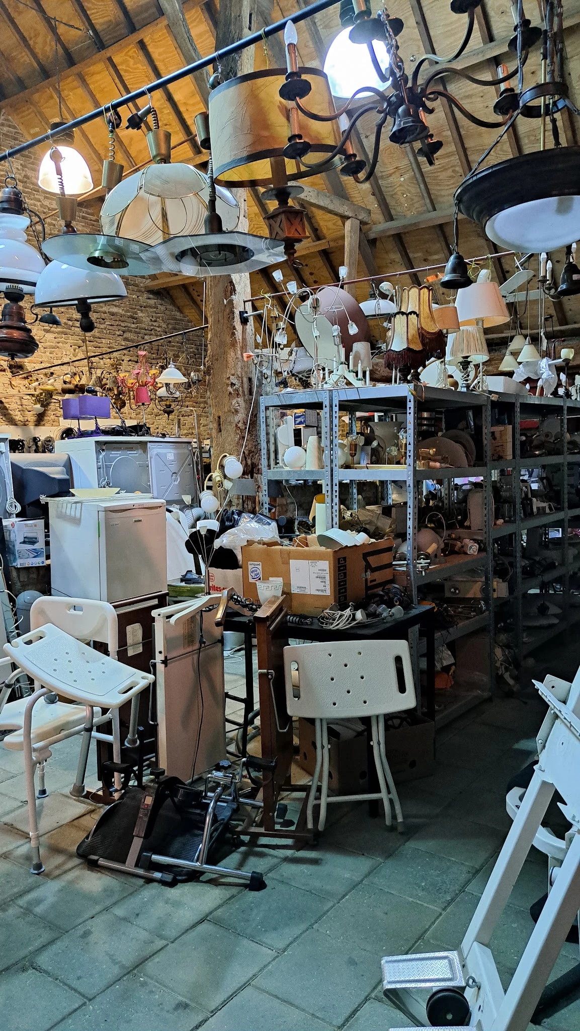 Rommelig interieur van kringloopwinkel met huishoudapparatuur, dozen, lampen en meubels