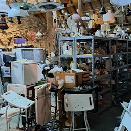 Rommelig interieur van kringloopwinkel met huishoudapparatuur, dozen, lampen en meubels