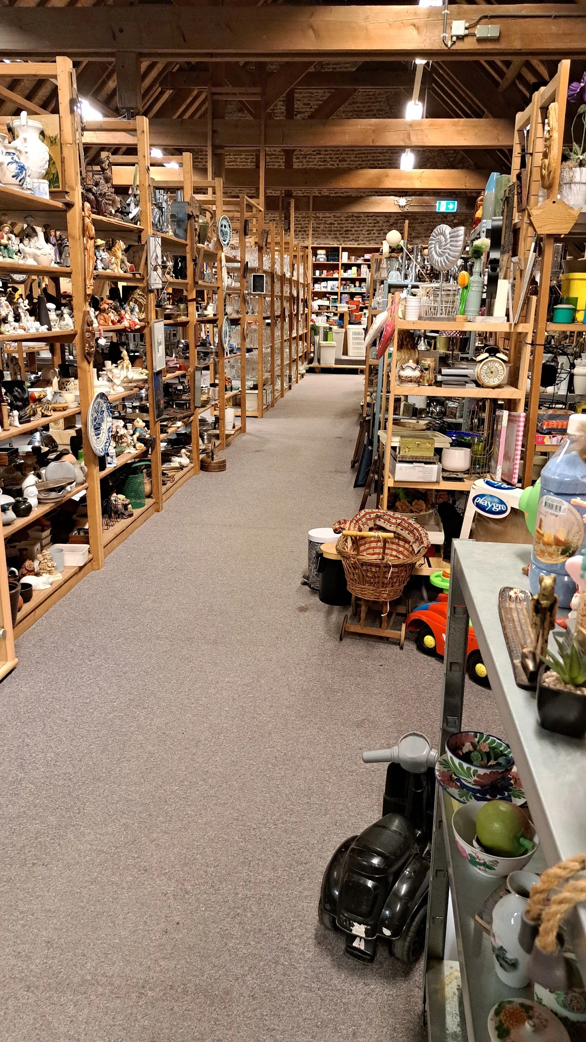 Winkelpad tussen houten stellingen met huishoudelijke spullen en decoratiematerialen in een kringloopwinkel