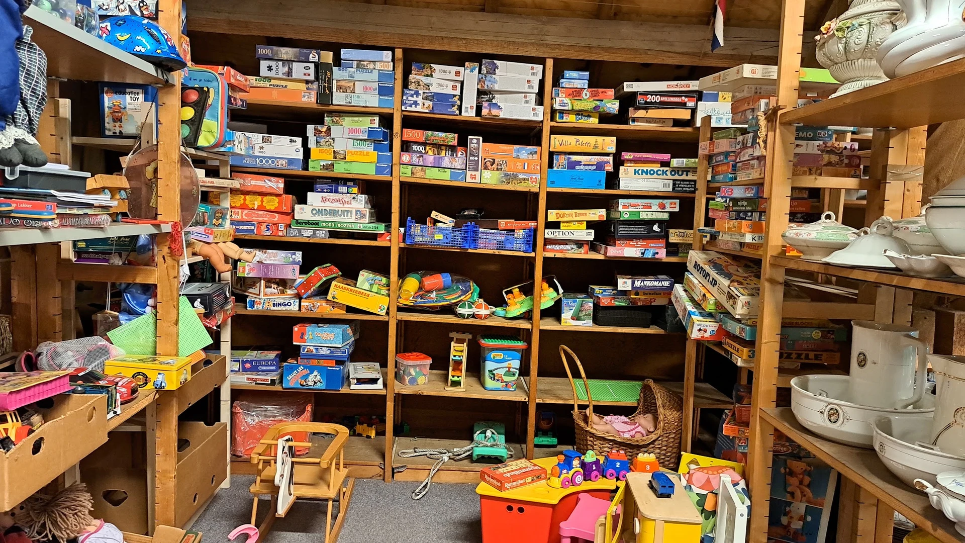 Houten stellingen volgeladen met dozen speelgoed, spellen en kinderartikelen in een kringloopwinkel