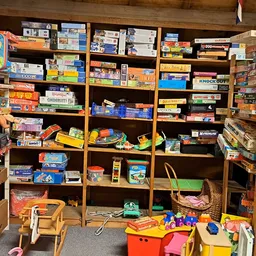Houten stellingen volgeladen met dozen speelgoed, spellen en kinderartikelen in een kringloopwinkel