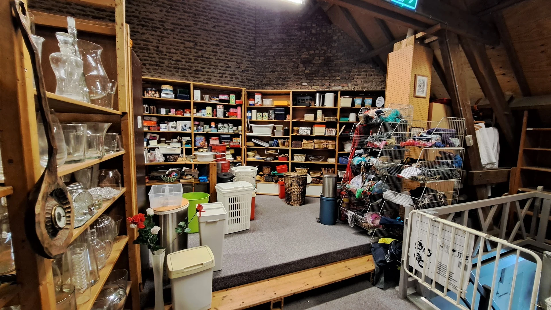Ruim winkelinterieur met houten stellingen vol spullen, winkelwagentjes en dozen met artikelen