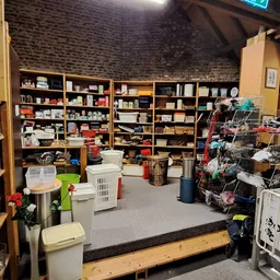 Ruim winkelinterieur met houten stellingen vol spullen, winkelwagentjes en dozen met artikelen