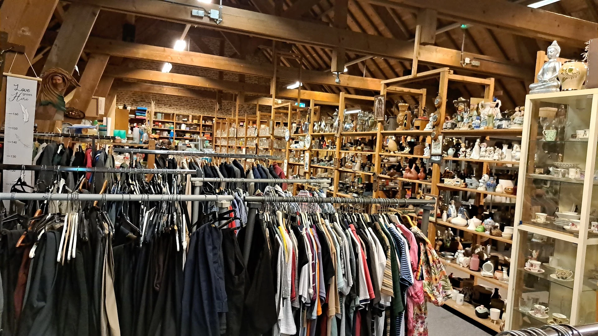 Interieur van kringloopwinkel met rekken tweedehands kleding en houten kasten met huishoudwaar en decoraties
