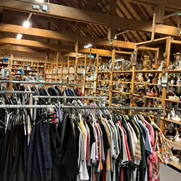 Interieur van kringloopwinkel met rekken tweedehands kleding en houten kasten met huishoudwaar en decoraties