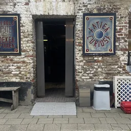 Ingang van kringloopwinkel met twee borden aan bakstenen gevel, bank links en diverse items op straat