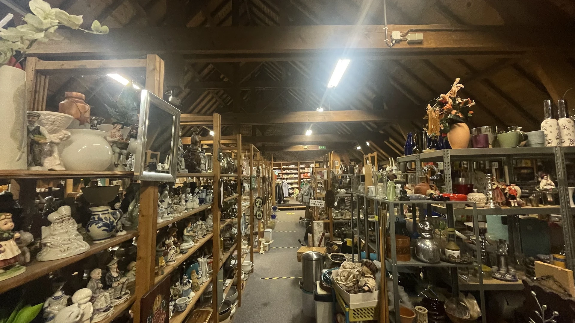 Binnenruimte van kringloopwinkel met lange gangpad en houten stellingen vol decoratieve voorwerpen, vazen en huishoudartikele