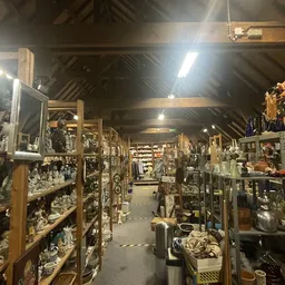 Binnenruimte van kringloopwinkel met lange gangpad en houten stellingen vol decoratieve voorwerpen, vazen en huishoudartikele