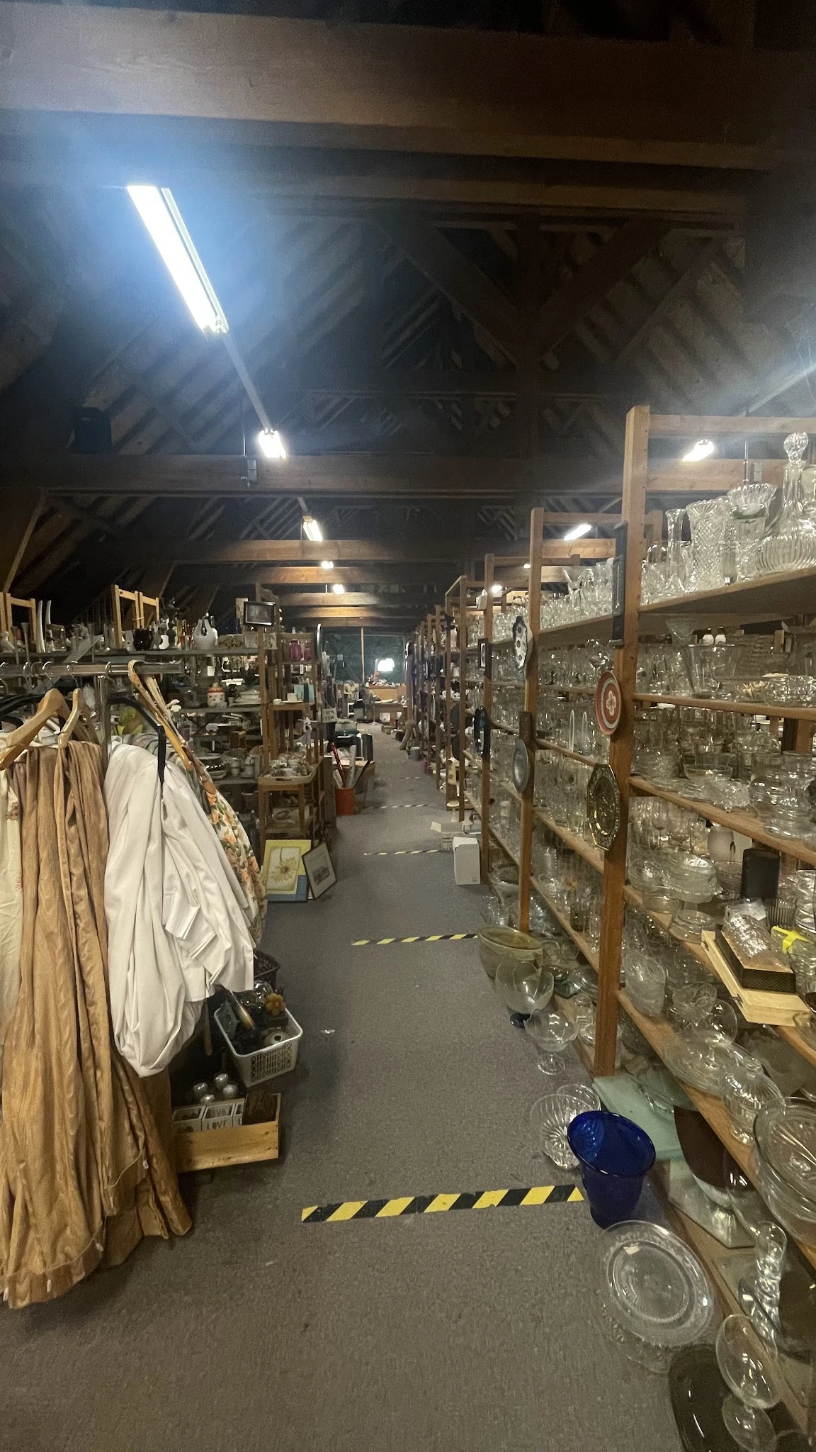 Binnenkant kringloopwinkel met stellingen vol glaswerk en servies rechts, kleding links, goed verlicht