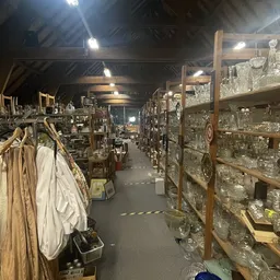 Binnenkant kringloopwinkel met stellingen vol glaswerk en servies rechts, kleding links, goed verlicht