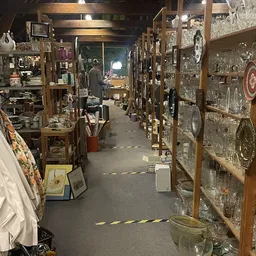Winkelinterieur met houten stellingen vol glaswerk en porselein langs beide zijden van het gangpad