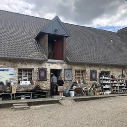 Stenen kringloopwinkel met steile daken, uitgestalde spullen op het terras ervoor