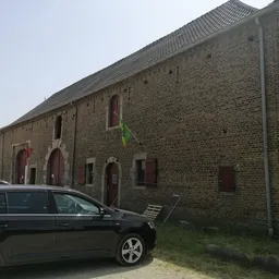 Bakstenen gevel van een kringloopwinkel met rode deuren en ramen, auto geparkeerd ervoor