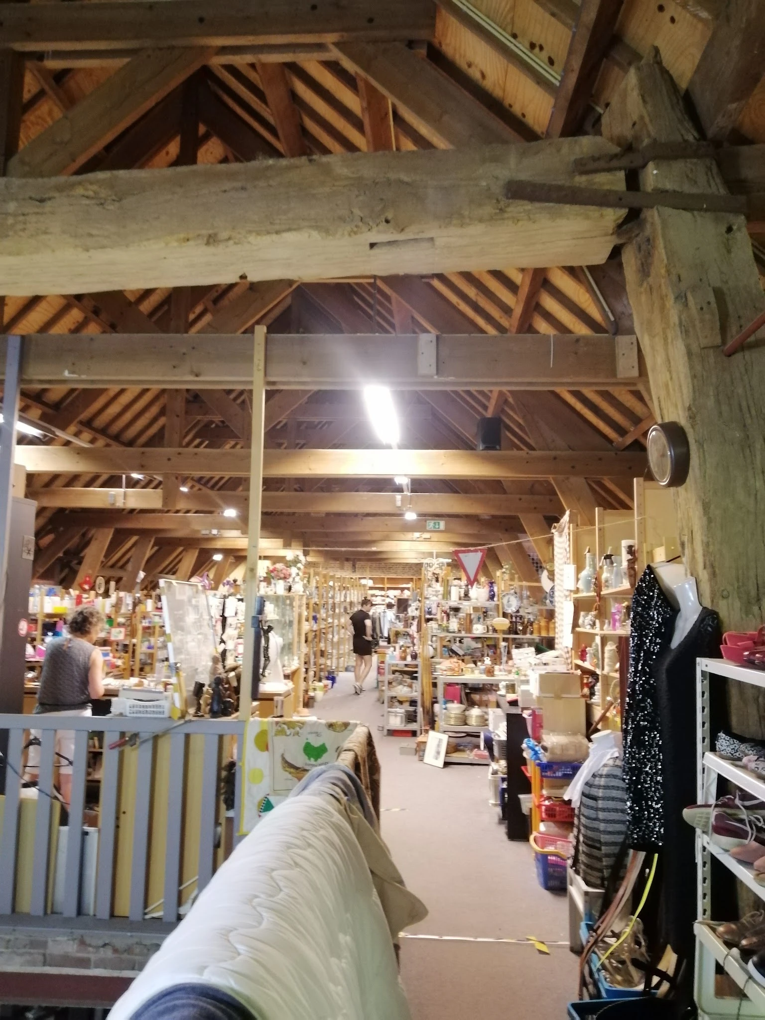 Overzicht van de winkelvloer met houten zoldering, stellingen vol spullen en diverse afdeling in een kringloopwinkel