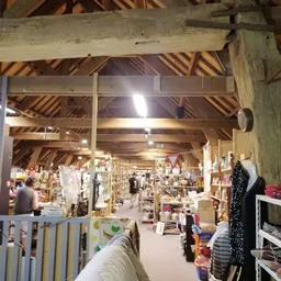 Overzicht van de winkelvloer met houten zoldering, stellingen vol spullen en diverse afdeling in een kringloopwinkel