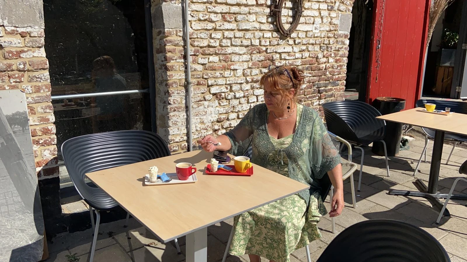 Vrouw zit aan tafel op het terras met koffie en gebak