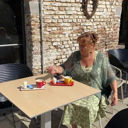 Vrouw zit aan tafel op het terras met koffie en gebak