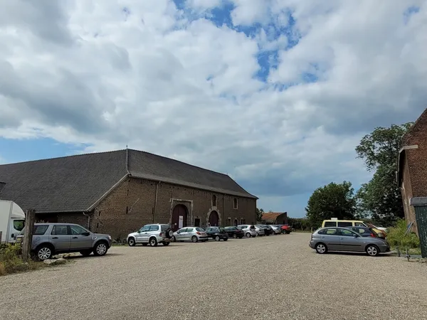 Bakstenen kringloopwinkel met parkeerplaats en geparkeerde auto's op zonnige dag