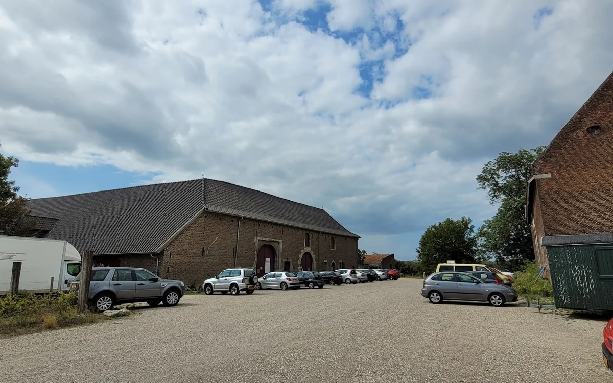 Bakstenen kringloopwinkel met parkeerplaats en geparkeerde auto's op zonnige dag