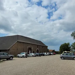 Bakstenen kringloopwinkel met parkeerplaats en geparkeerde auto's op zonnige dag