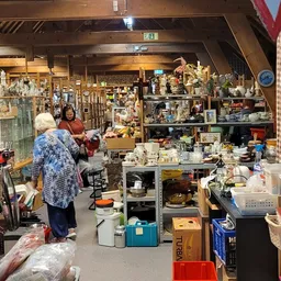 Winkelvloer van kringloopwinkel met diverse uitgestalde spullen, stellingen, dozen en bezoekers