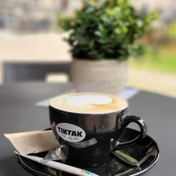 Cappuccino met latte art in zwart TIKTAK-kopje op schotel buiten