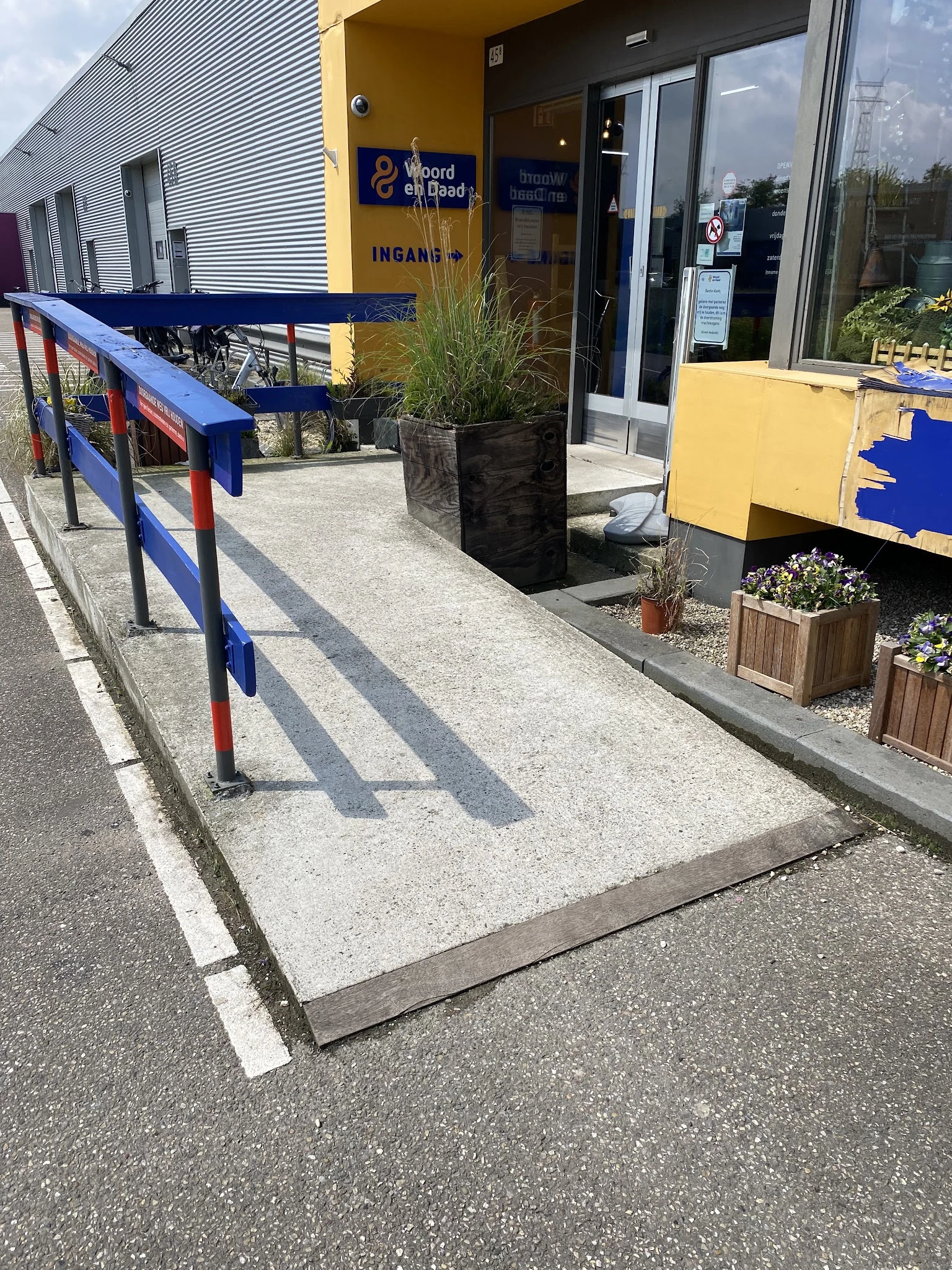 Toegangspad met blauwe reling naar winkelingang met gele en blauwe elementen