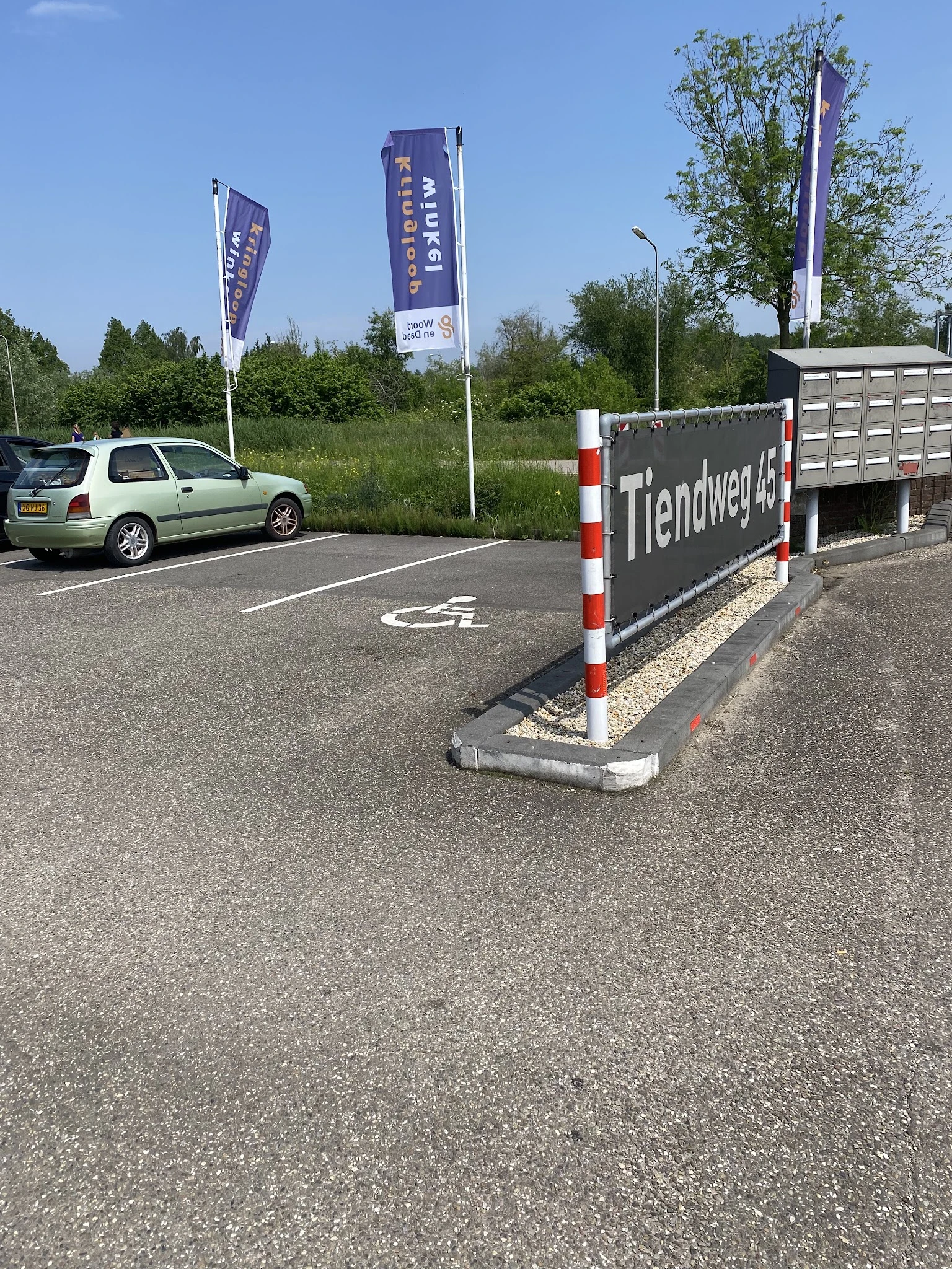 Parkeerplaats met auto en reclamebord van kringloopwinkel aan Tiendweg