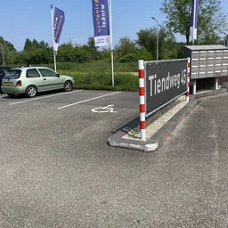 Parkeerplaats met auto en reclamebord van kringloopwinkel aan Tiendweg