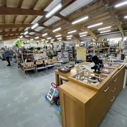 Overzicht van de winkelvloer met stellingen, toonbanken en uiteenlopende tweedehands spullen in een groot magazijn met houten