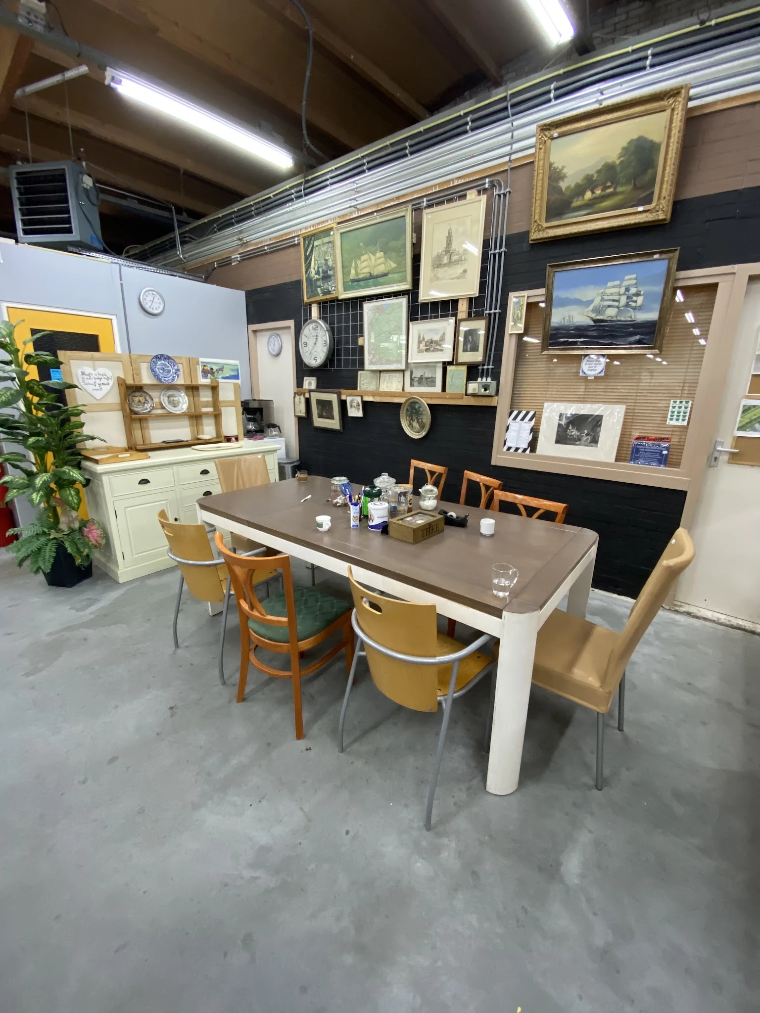 Winkelbinnenruimte met eettafel en stoelen, stellingen met schilderijen en decoratie aan de muren