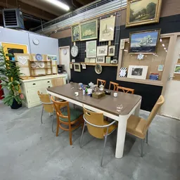 Winkelbinnenruimte met eettafel en stoelen, stellingen met schilderijen en decoratie aan de muren