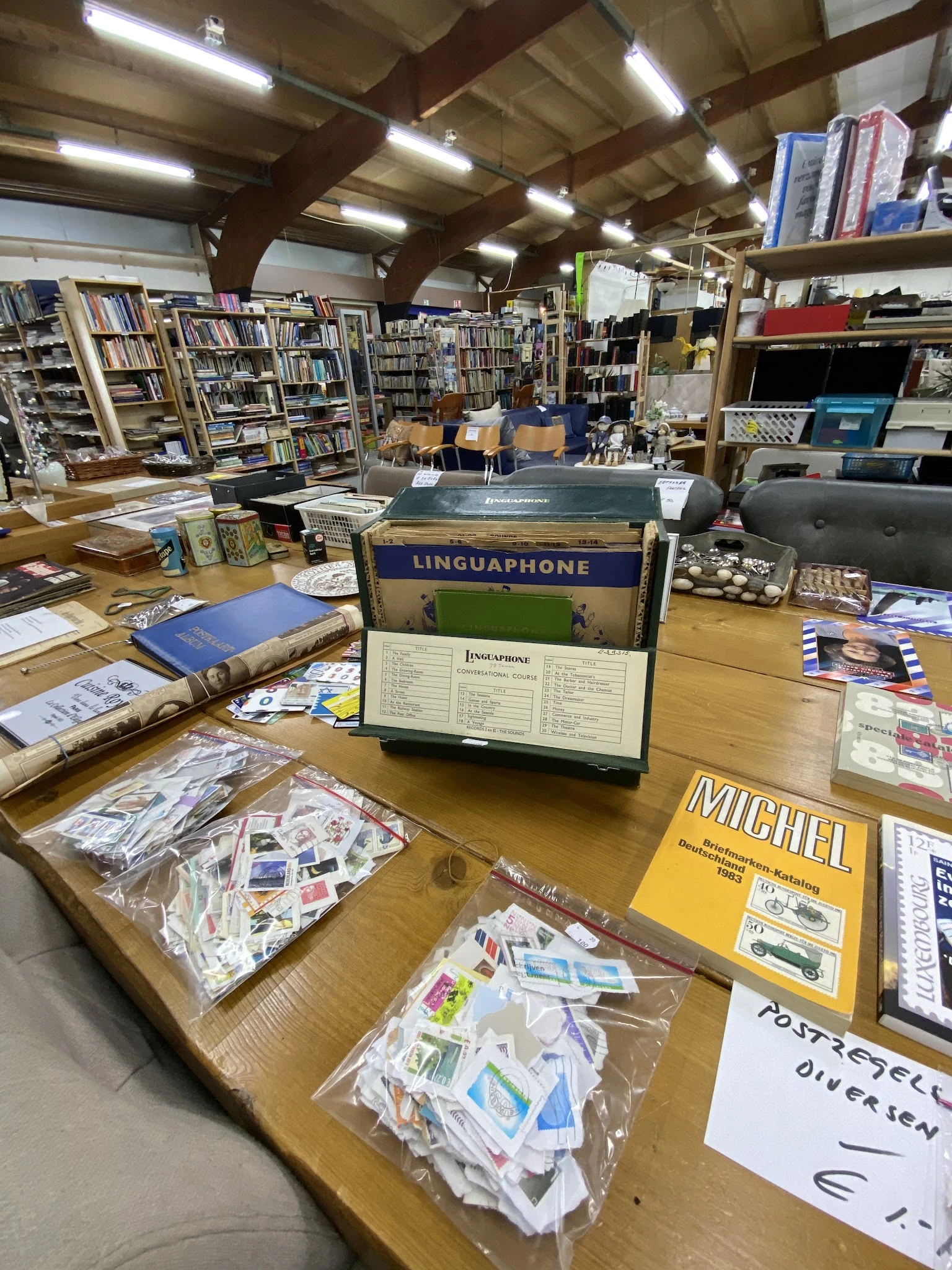 Houten tafel met diverse tweedehands boeken, postzegels, een Linguaphone-taalcursus en andere curiosa in een kringloopwinkel