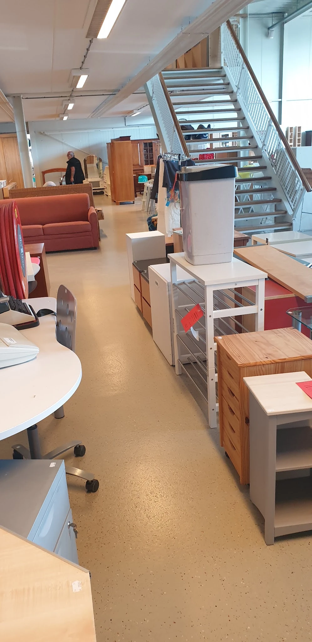 Winkelvloer met diverse meubels waaronder houten kasten, witte stellingen met grijze deuren, ronde tafels en rood/roze textie
